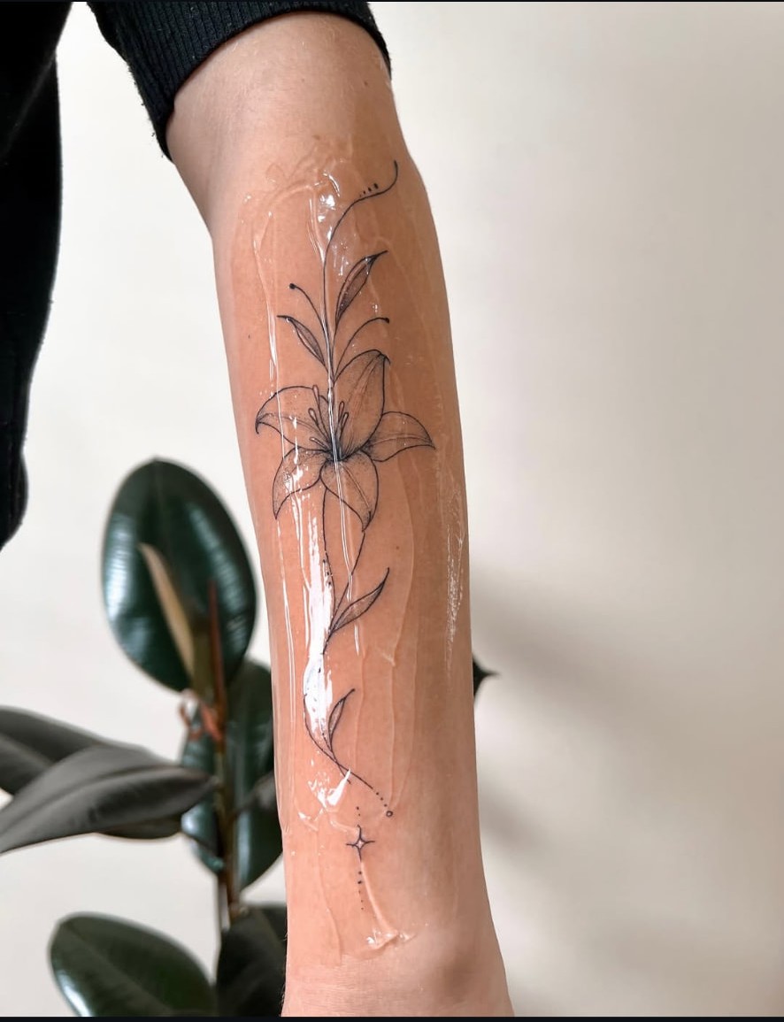 Tatuagem floral fine line de lírio no antebraço