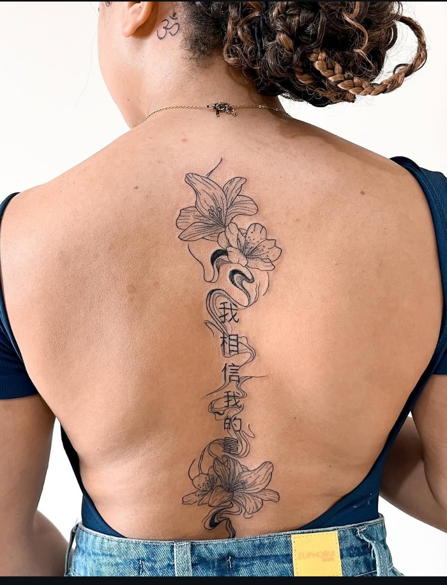 Tatuagem floral com escrita oriental na coluna